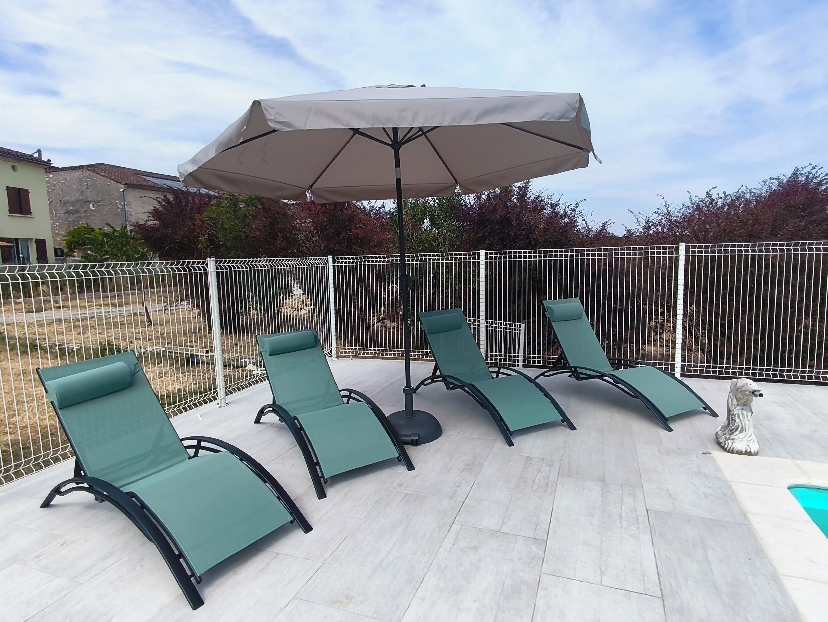Eine Terrasse mit vier Liegestühlen und einem großen Sonnenschirm.