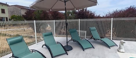 Eine Terrasse mit vier Liegestühlen und einem großen Sonnenschirm.