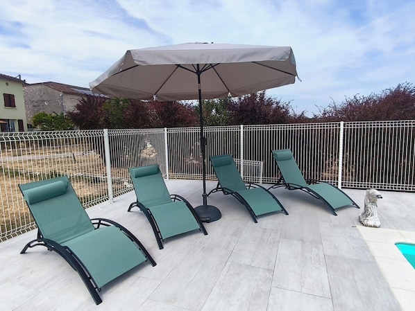 A patio with four lounge chairs and a large umbrella.