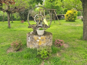 A garden with a metal sculpture, a potted plant, and a swing set.