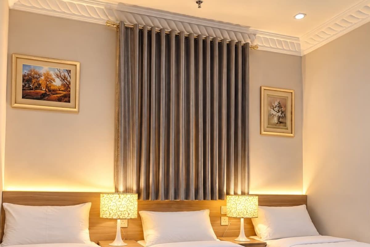 A hotel room with three beds, a large window with curtains, and two wall-mounted lamps.