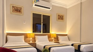 A hotel room with two beds, a red chair, a small round table, and an air conditioning unit. - Sakab Al Aseel Hotel  (Makkah)