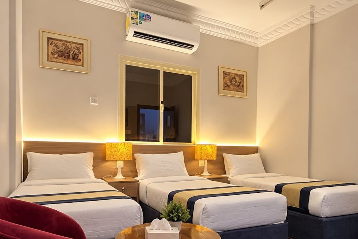 A hotel room with two beds, a red chair, a small round table, and an air conditioning unit.