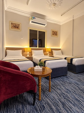 A hotel room with two beds, a red chair, a small round table, and an air conditioning unit. - Sakab Al Aseel Hotel  (Makkah)