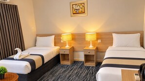 A hotel room with two beds, a small table, a chair, a potted plant, and a painting on the wall. - Sakab Al Aseel Hotel  (Makkah)