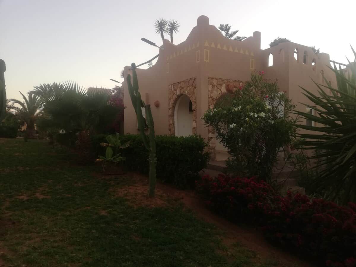 A building with a desert-style facade, arched entrance, and surrounded by cacti and flowering plants.