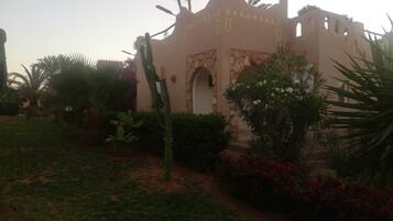 A building with a desert-style facade, arched entrance, and surrounded by cacti and flowering plants.