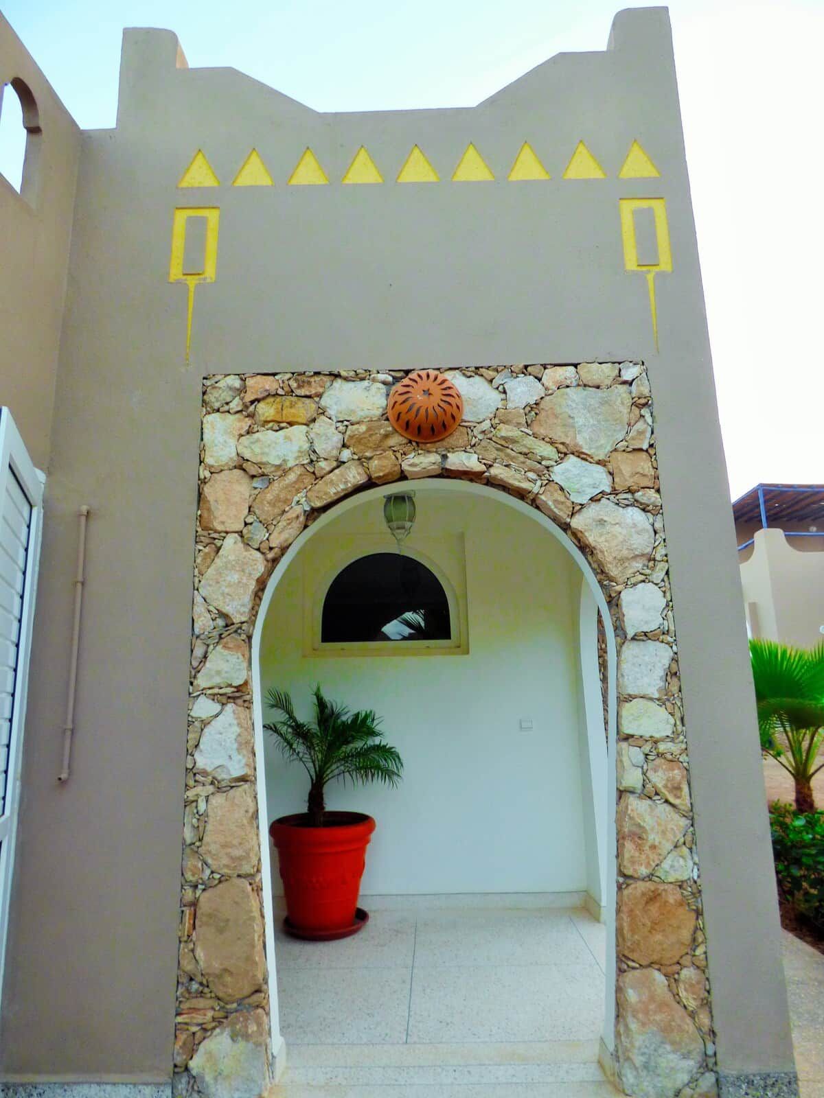 Une entrée d’immeuble avec une arche en pierre, un pot de fleurs et un élément décoratif au-dessus de l’arche.