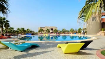 Una piscina con sillas de descanso, palmeras y un edificio al fondo.