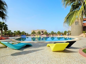 A swimming pool with lounge chairs, palm trees, and a building in the background. - Villa Club Evasion, Right on the Atlantic and Pool Access (Mirleft)