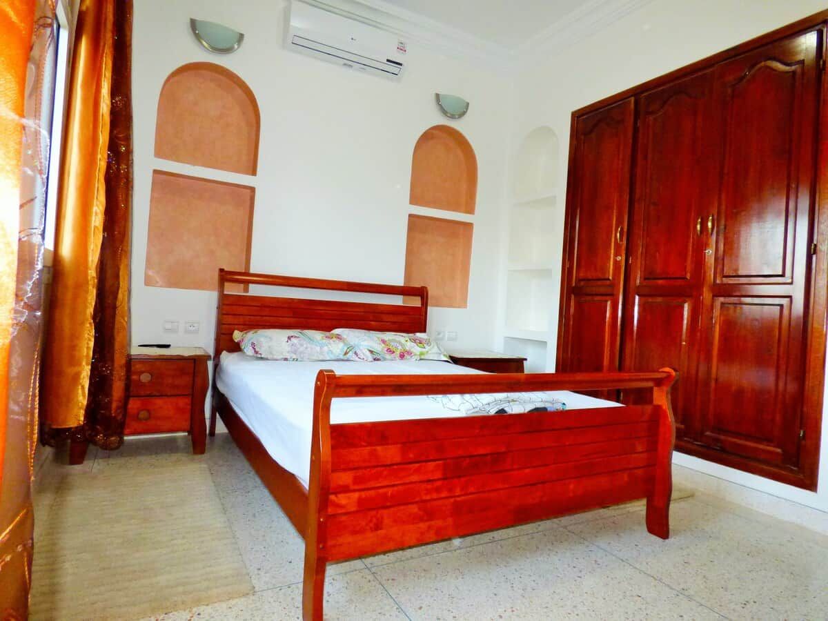 Un dormitorio con una cama de madera, una mesita de noche, un armario y aire acondicionado instalado en la pared.