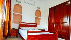 Quarto com cama de madeira, mesa de cabeceira, guarda-roupa e ar condicionado fixado na parede.