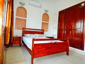 A bedroom with a wooden bed, a nightstand, a wardrobe, and a wall-mounted air conditioner. - Villa Club Evasion, Right on the Atlantic and Pool Access (Mirleft)
