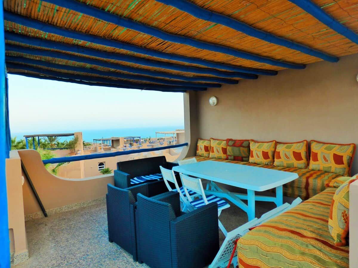 A room with a table and chairs, a sofa, and a view of the beach and ocean.