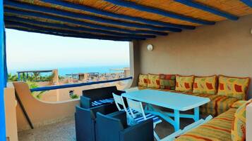 A room with a table and chairs, a sofa, and a view of the beach and ocean.