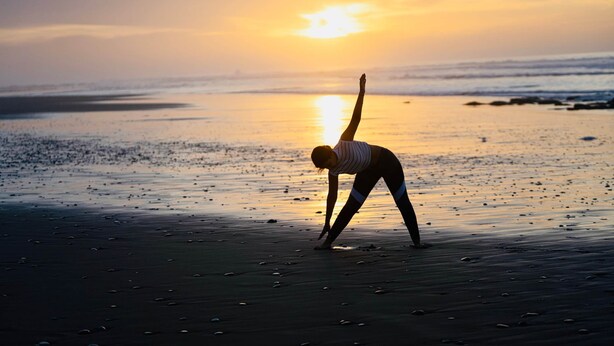 Uma pessoa fazendo uma postura de yoga na praia ao pôr do sol.