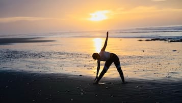 Una persona realizando una postura de yoga en la playa al atardecer.