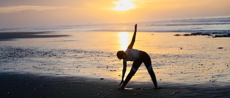 A person performing a yoga pose on a beach at sunset.
