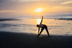 A person performing a yoga pose on a beach at sunset.