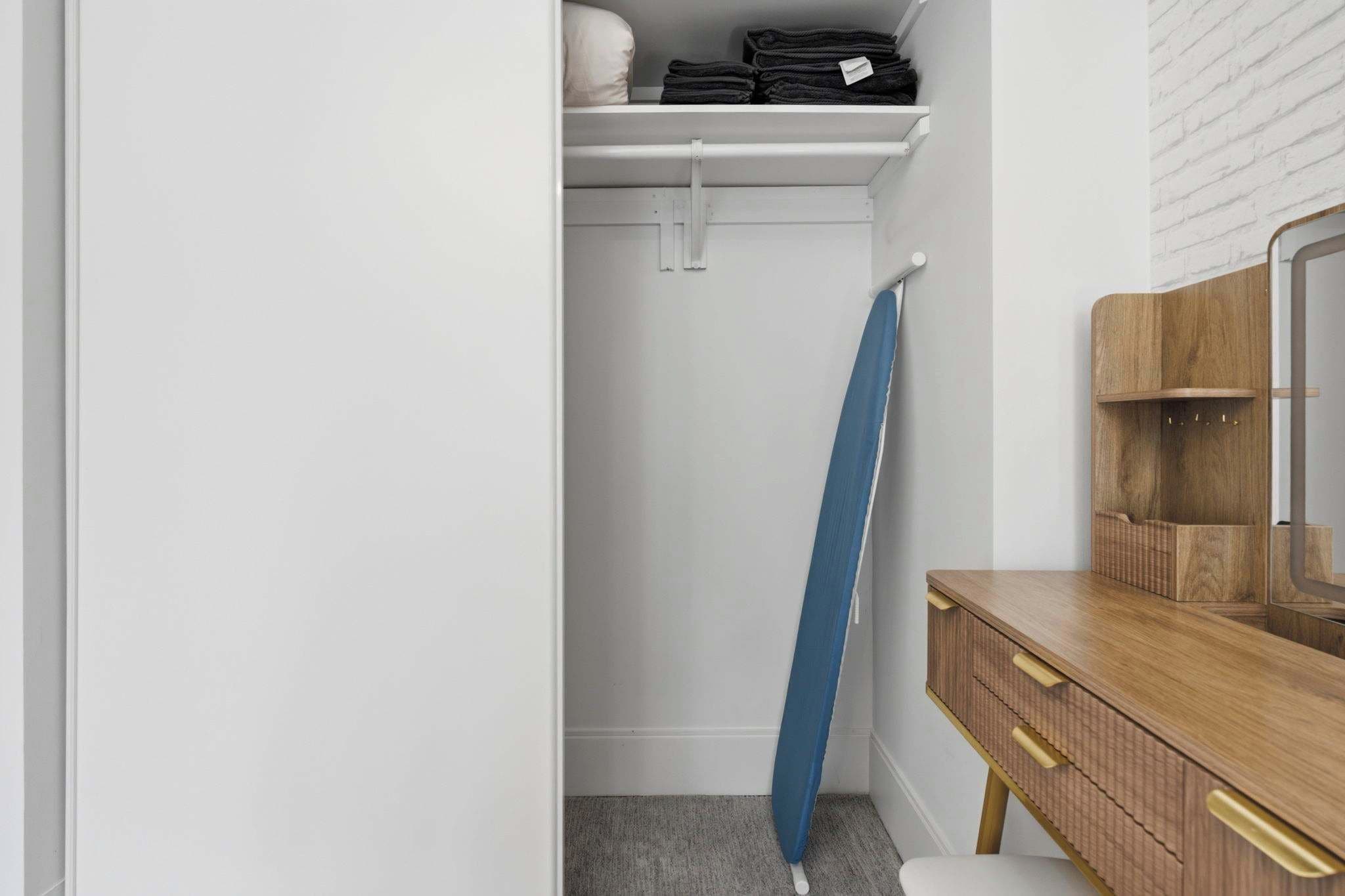 A closet with a hanging rod, a folded blue garment, and a wooden dresser with a mirror.