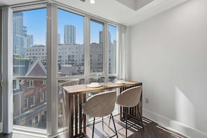 Eine hohe Wohnung mit Essbereich, inklusive Holztisch und zwei Stühlen, große Fenster mit Blick auf die Stadt.