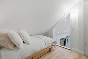 A bedroom with a sloped ceiling, a bed with pillows, and a wooden floor.