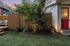 A residential backyard with a wooden fence, a small tree, and a red door.