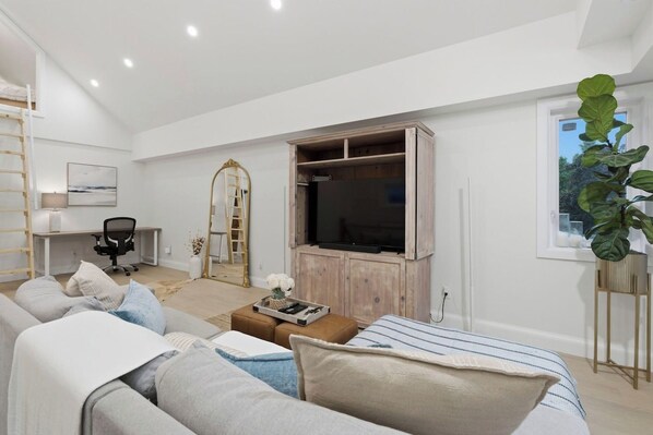 A modern living room with a large flat-screen TV, a sofa set, a coffee table, and a plant.