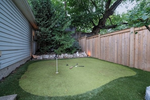 A backyard with artificial turf, a wooden fence, and a tree.
