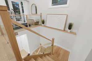 A modern interior with a wooden staircase, a glass railing, and a view of a balcony.