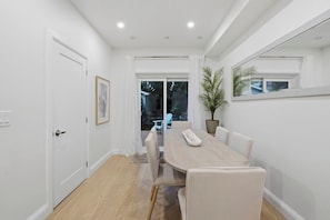 A dining area with a long table and chairs, a potted plant, and a view of the outdoors.