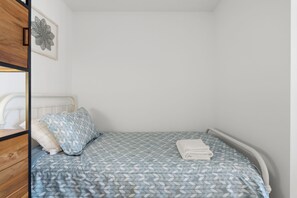 Ein Einzelbett mit blattgemusterten Bettdecken und Kissen, ein weißes Kopfstück und ein Wandbild.