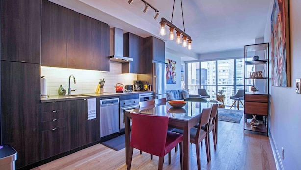 Cocina moderna con armarios de madera oscura, un refrigerador de acero inoxidable y una zona de comedor con una silla roja.
