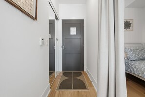 Ein Flur, der zu einem Schlafzimmer mit Bett, Tür und einem an der Wand befestigten Lichtschalter führt.