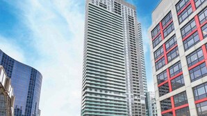 Un edificio alto y moderno con fachada de entramado, rodeado de otros edificios y una calle concurrida.