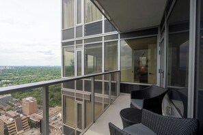 A balcony with a view of a cityscape, featuring a glass railing and wicker furniture. - 2BR Yorkville Retreat - Balcony & Views (Toronto)