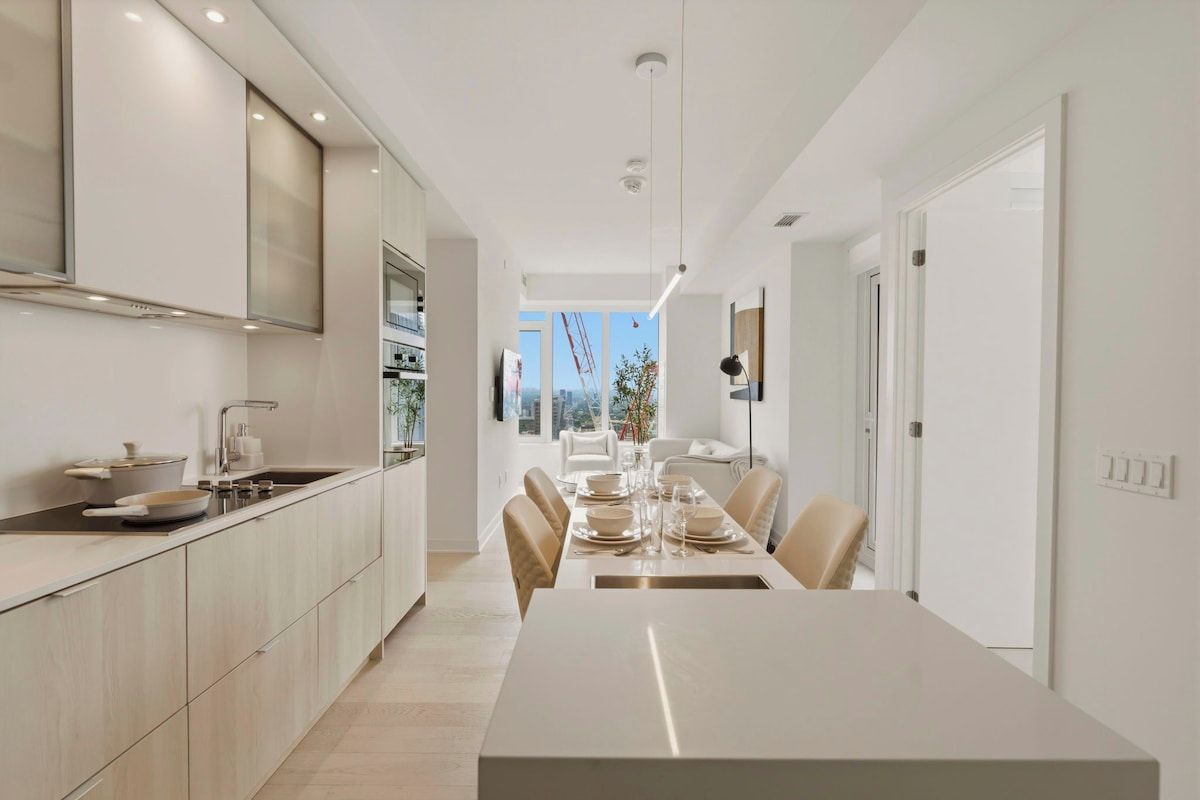 Una cocina moderna con comedor, que incluye una mesa larga y sillas, horno empotrado y vistas al exterior.