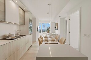 Una cocina moderna con comedor, que incluye una mesa larga y sillas, horno empotrado y vistas al exterior.