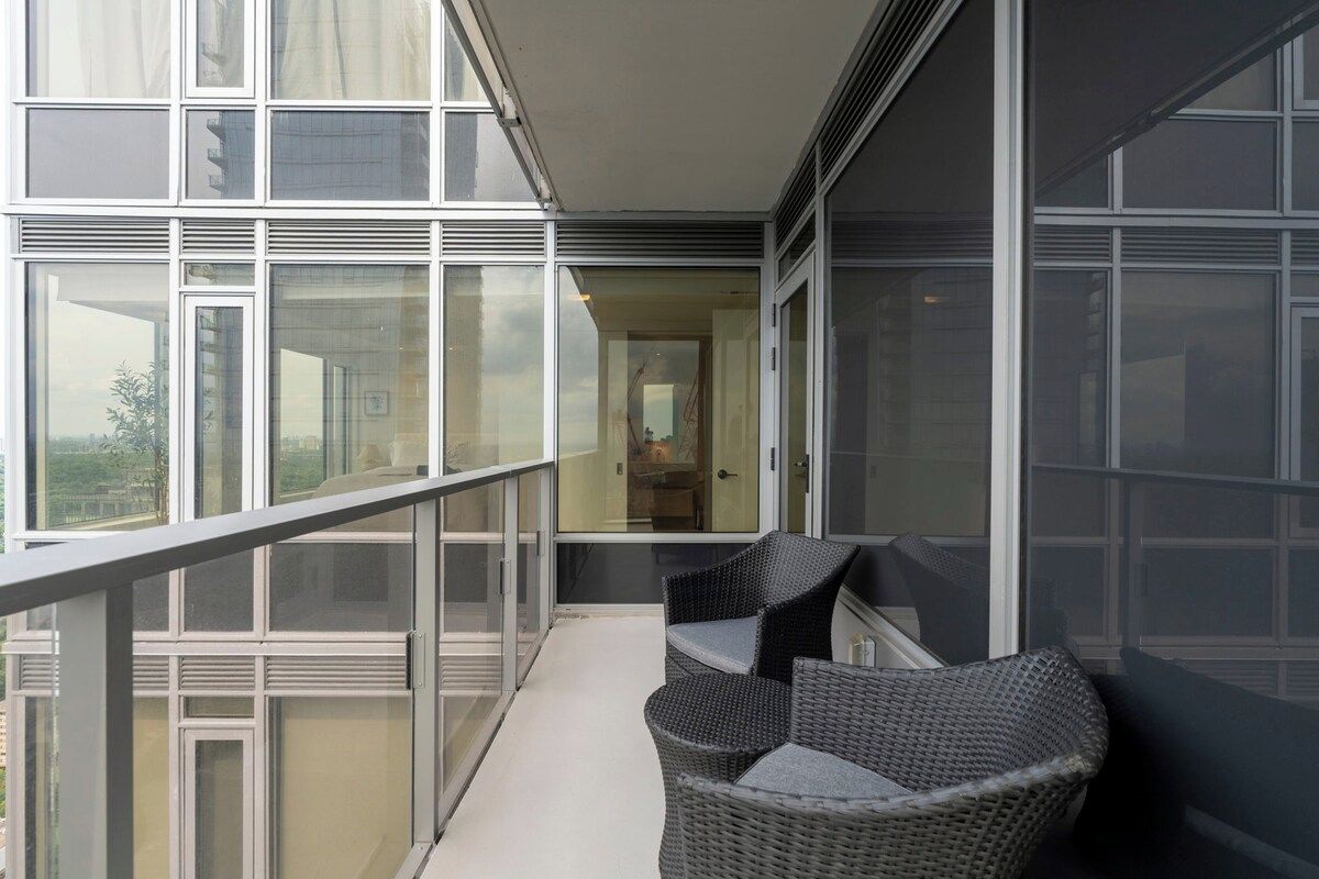 A balcony with a glass railing, wicker furniture, and a view of the cityscape.