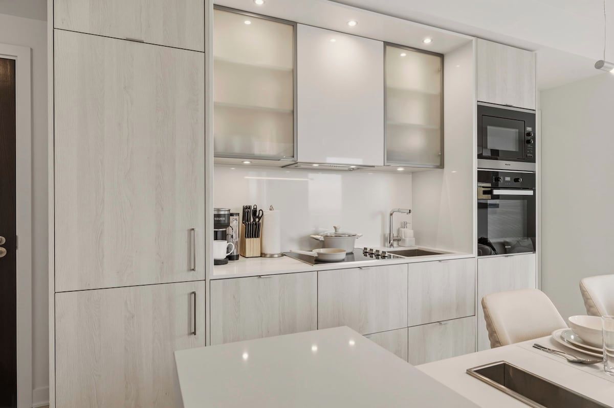 A modern kitchen with white cabinetry, a built-in oven, and a dining area with a white table.
