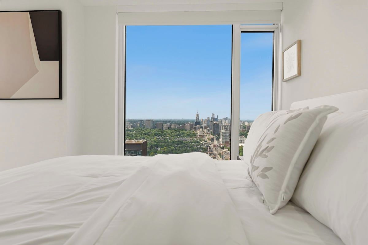 Habitación de hotel con cama, ventana grande y vista a la ciudad.
