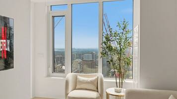 A modern living room with a large window, a sofa, a chair, and a small table with a plant.