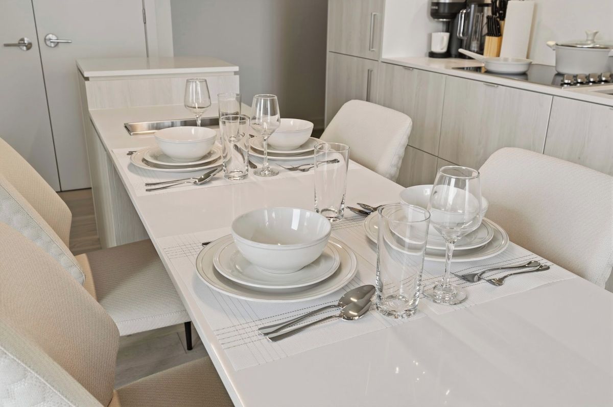 A dining area with a long table set for four, equipped with white plates, bowls, glasses, and cutlery.