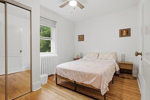 Une chambre à coucher avec un lit, des tables de chevet, une fenêtre et un ventilateur de plafond.