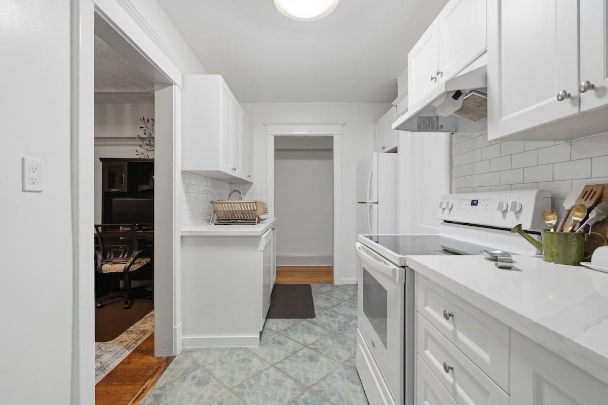 A kitchen with white cabinets, a stove, and a countertop with utensils.