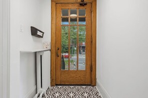 A wooden door with glass panels, a white wall, a small shelf with a picture frame, and a patterned floor.