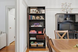 A dining area with a wooden table, chairs, a bookshelf with various items, and a television in the background.