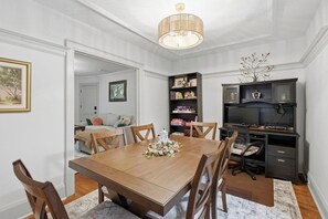 A dining area with a wooden table and chairs, a chandelier, a bookshelf, and a television.