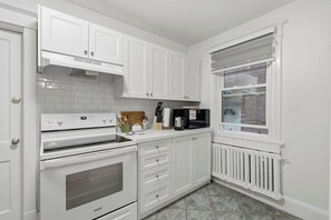 A kitchen with white cabinetry, a stove, oven, and a window with blinds.
