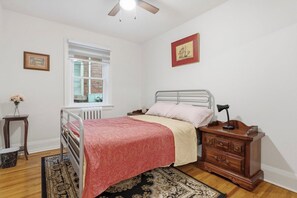 A bedroom with a bed, a nightstand, a dresser, a window with blinds, and a ceiling fan.